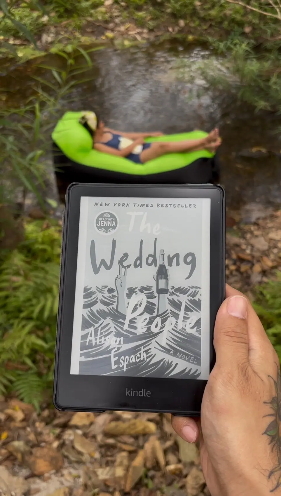 A person holding a Kindle displaying the cover of the book in an outdoor setting.