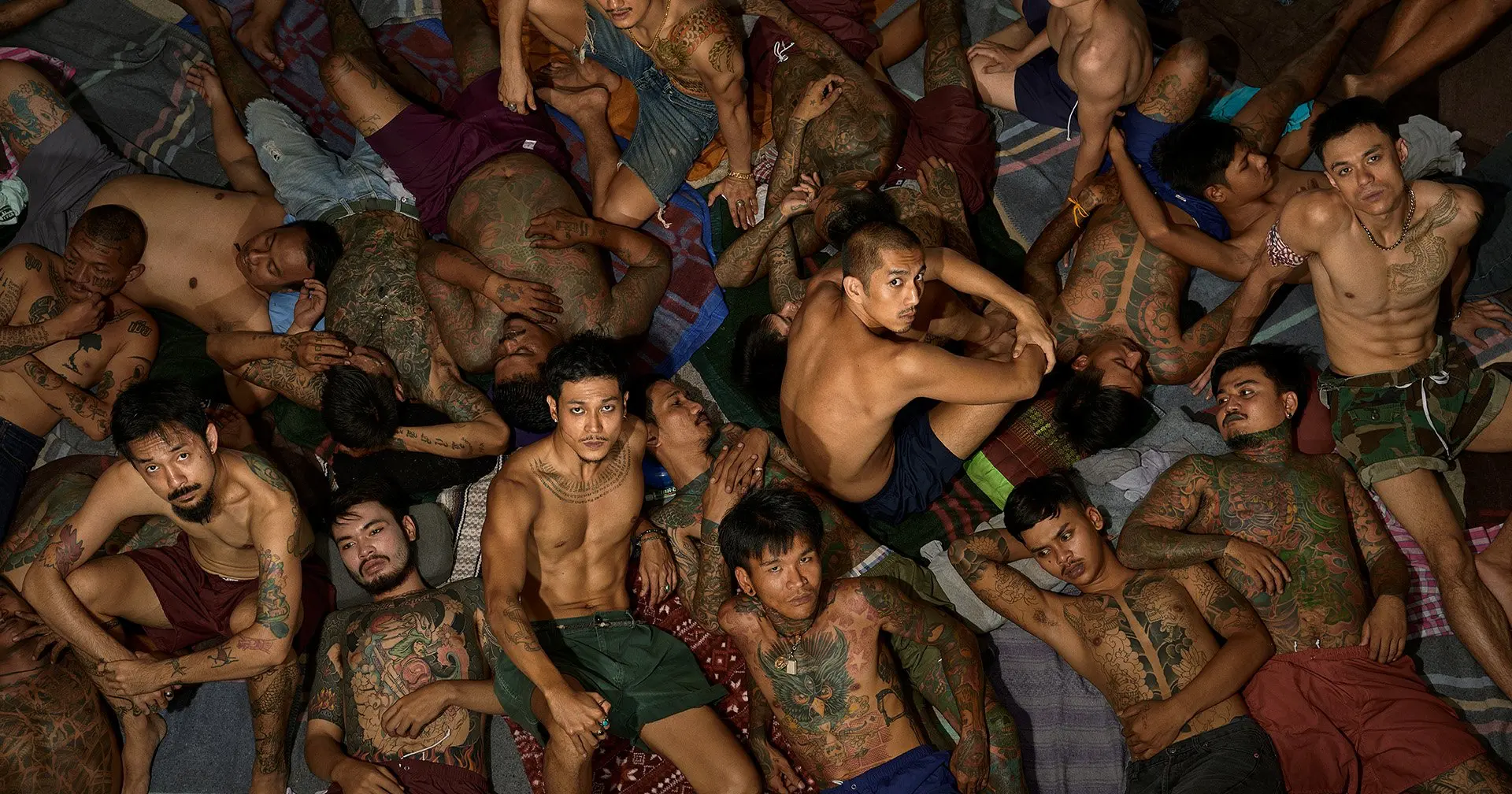 A crowded prison cell with inmates lying and sitting close together, showing tense and harsh conditions.